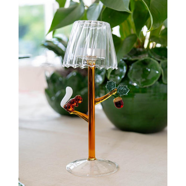 Decorative glass lamp with bird design on a white surface with green plants in the background