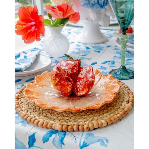 Pomegranate on an orange plate with a floral tablecloth and decorative glassware.