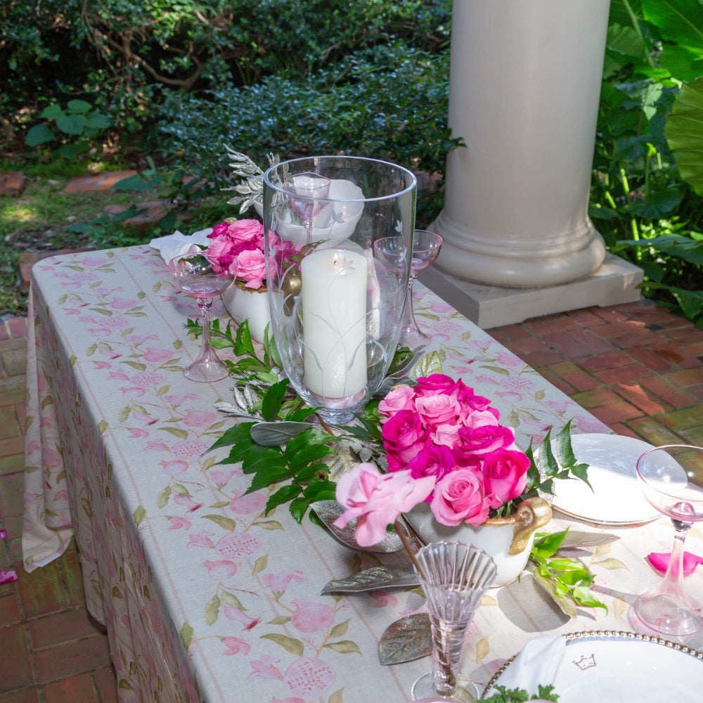 Decorative table setting with pink flowers, candles, and a floral tablecloth outdoors.
