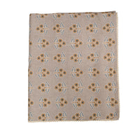 A square fabric folded tablecoth with a beige background, featuring a repeating block-print style floral pattern in brown, mustard yellow, and light blue.