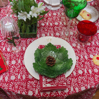 Decorative table setting with a green leaf-shaped plate on a red and white patterned tablecloth.