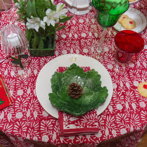 Decorative table setting with a green leaf-shaped plate on a red and white patterned tablecloth.