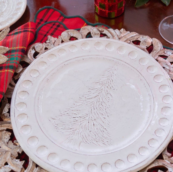 Decorative white plate with embossed design on a wooden surface with plaid fabric and red glassware.