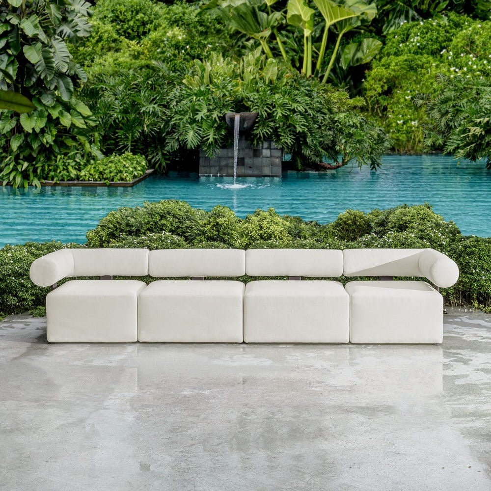 Modern white outdoor sofa in front of a pool with a waterfall and lush greenery.