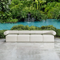 Modern white outdoor sofa in front of a pool with a waterfall and lush greenery.