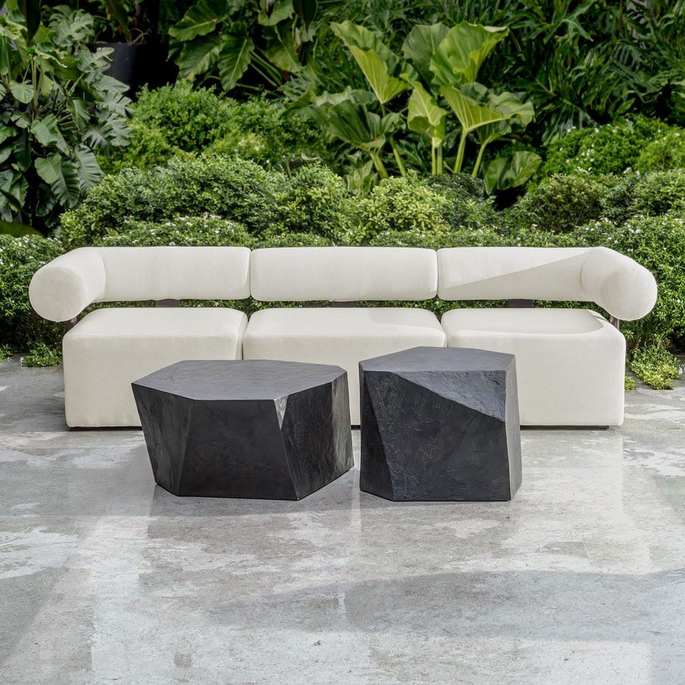 White outdoor sofa with two black stone tables against a green foliage background