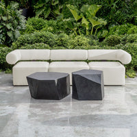 White outdoor sofa with two black stone tables against a green foliage background