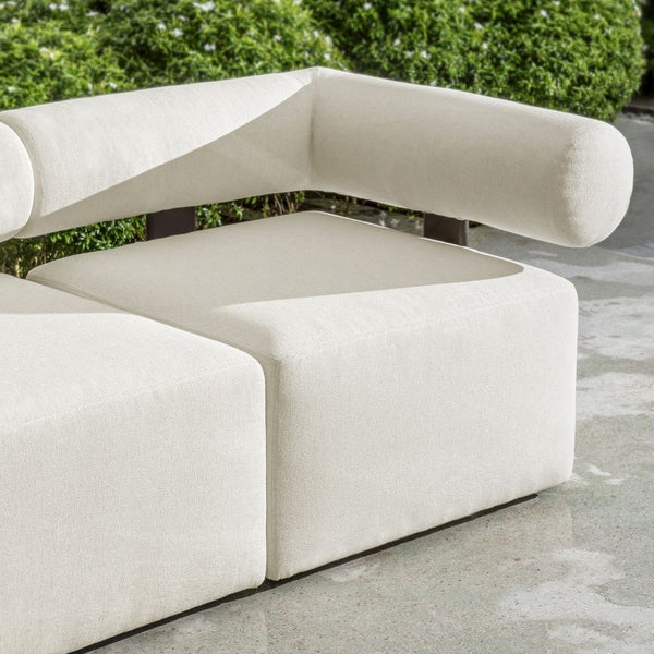 Modern beige sofa with curved design on a concrete surface with greenery in the background