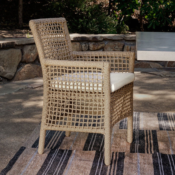 Wicker chair with a cushion on a patio with a stone wall and bench in the background.