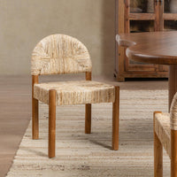 A wooden dining chair with a woven natural-fiber seat and curved backrest, shown in a styled dining room setting next to a wooden table.