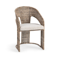 A wicker dining chair with a curved backrest, armrests, and a light beige textured seat cushion, shown against a plain white background.
