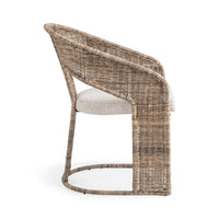 A modern wicker armchair with a curved backrest, woven in natural brown and beige tones, featuring a light beige upholstered seat cushion, shown from a three-quarters angle on a white background.