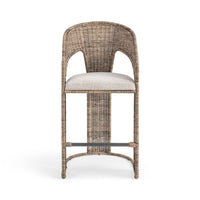 A tall wicker barstool with a curved backrest, upholstered light beige seat cushion, and a dark metal footrest bar, shown against a plain white background.