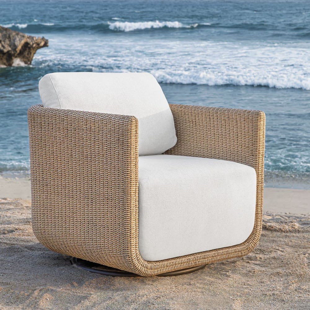 Wicker chair with white cushions on a sandy beach with ocean waves in the background