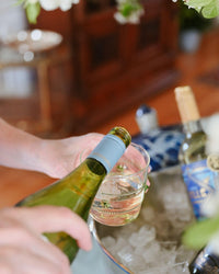Person pouring white wine into a glass with a blurred background