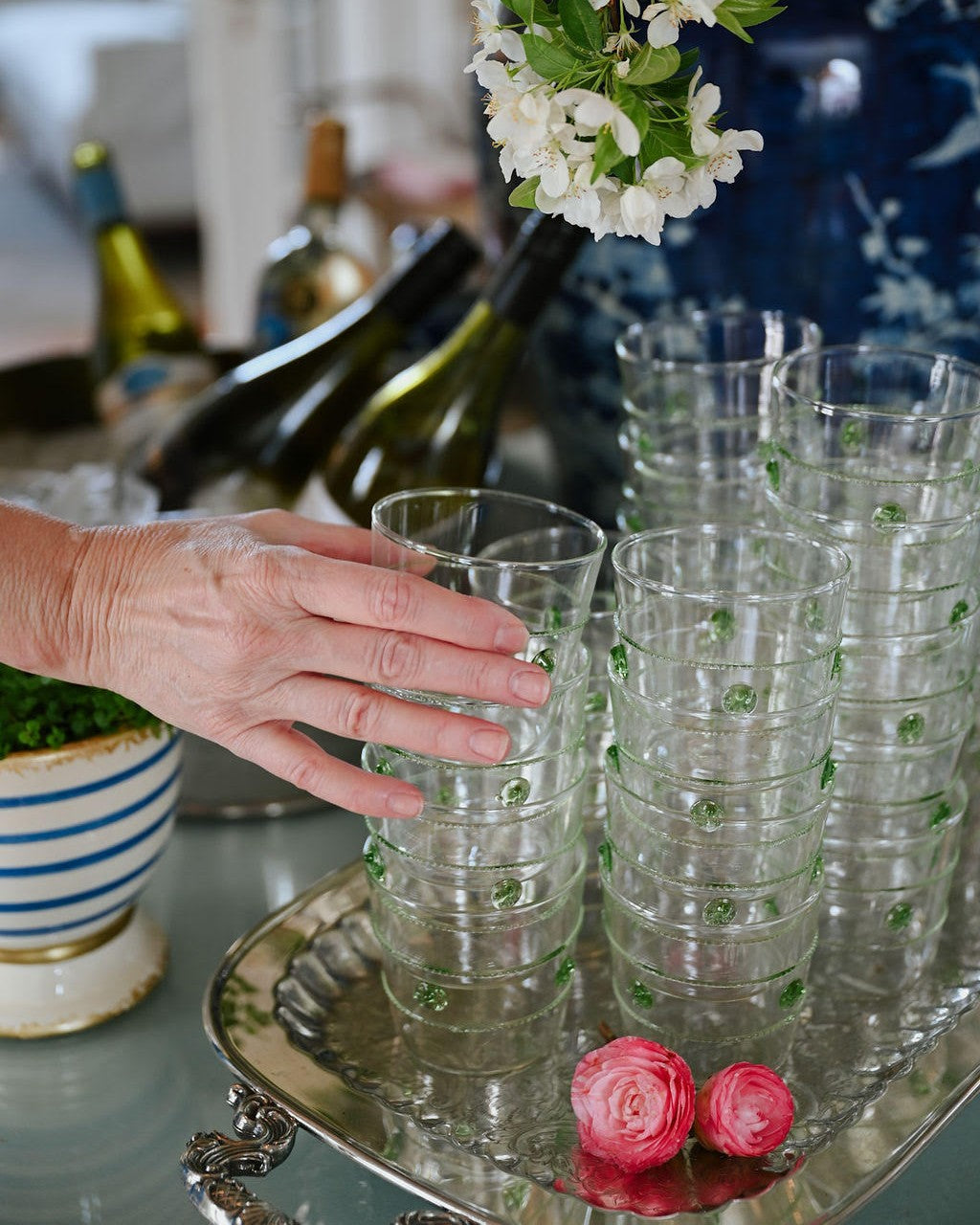 Stacks of clear glasses with green dots on a tray, with a hand reaching out to pick one up.