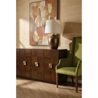 A dark brown wooden sideboard cabinet with geometric paneling and square knobs, styled in a room next to an olive green armchair and a table lamp, with a large abstract painting on the textured beige wall behind it.