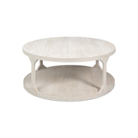 A round, low-profile coffee table with a whitewashed light wood finish, featuring a top surface, a lower shelf, and four angled support legs.