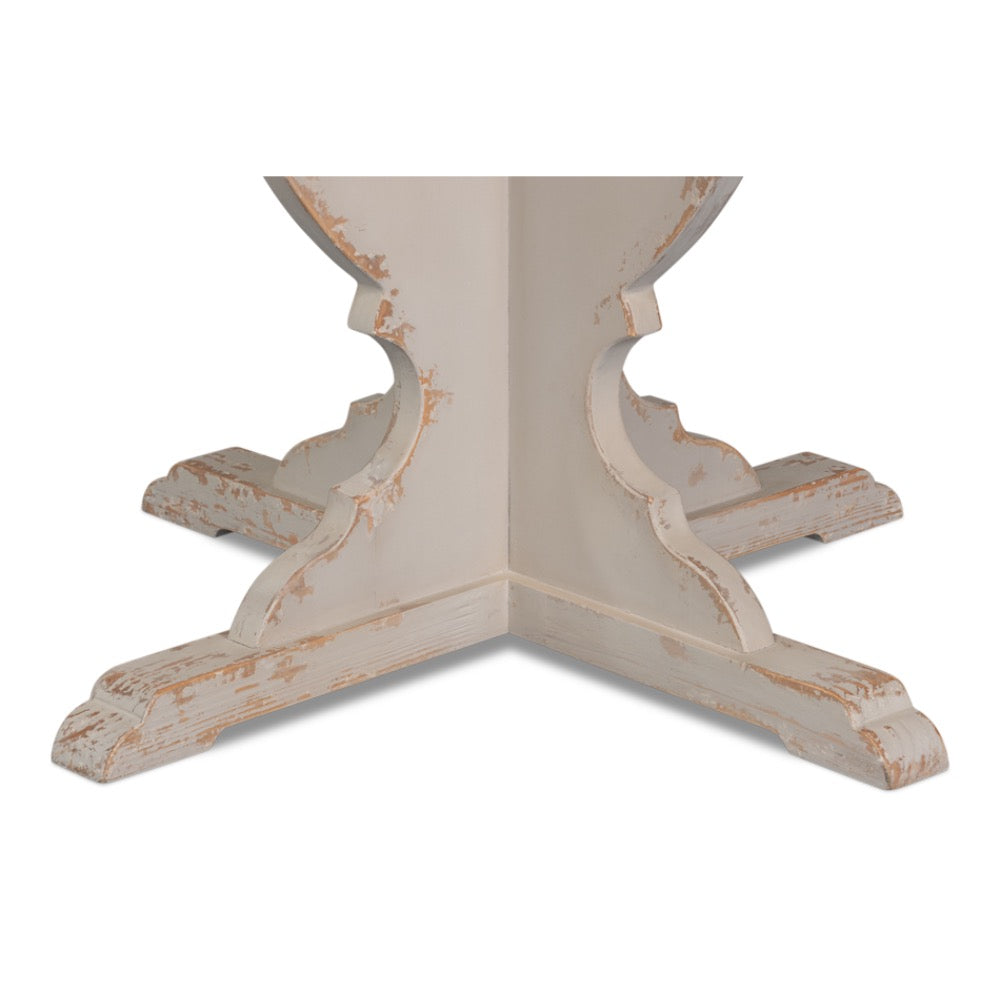A close-up of a distressed white wooden table base with a scalloped central post and four supporting legs, showing a weathered tan finish on a white background.