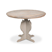 A round dining table with a distressed light wood top and a carved pedestal base in a light gray finish, shown on a white background.