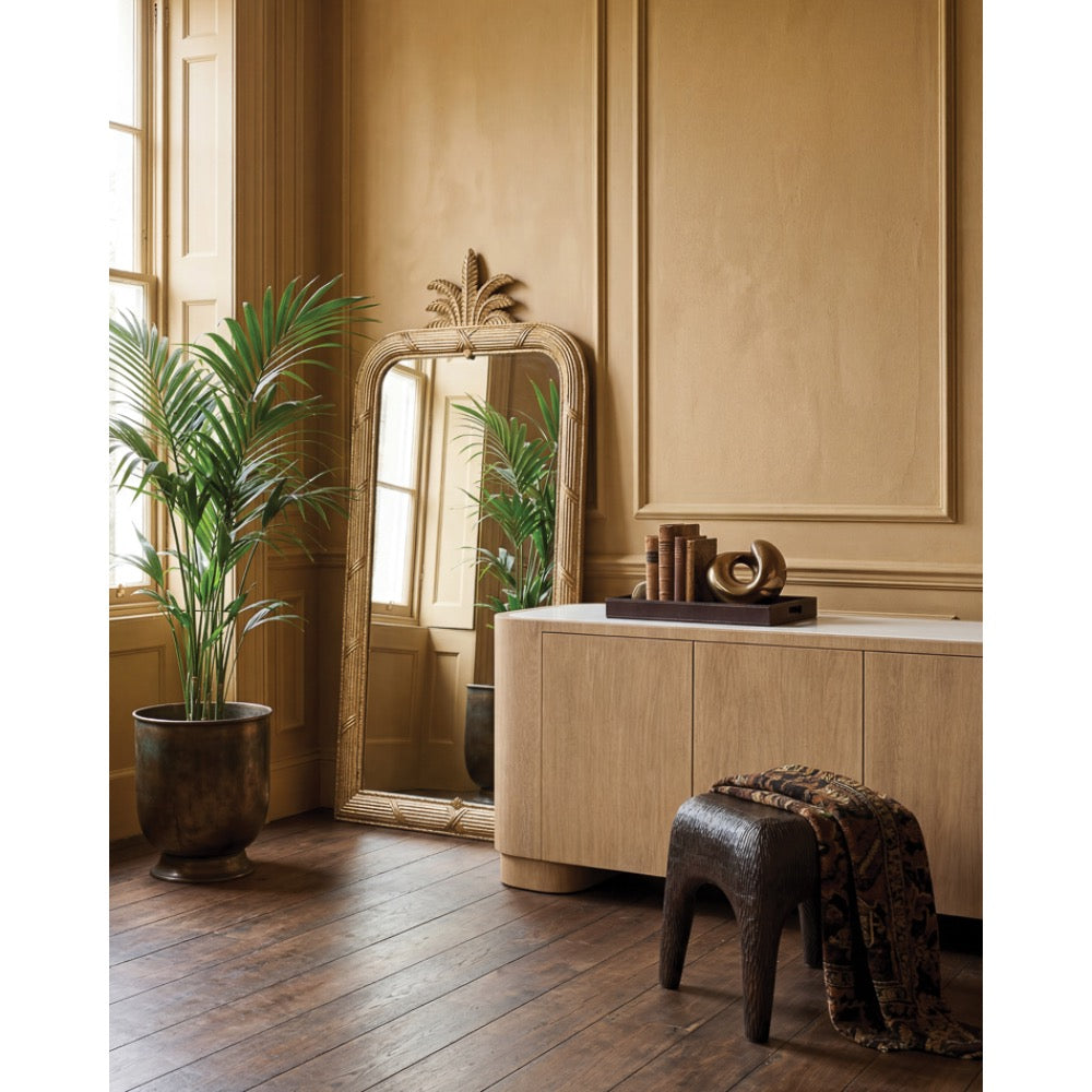 gold rounded rectangular mirror pinapple leaf accent top wood sideboard and potted plant and stool in background