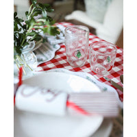 Decorative table setting with glasses, plates, and a plant on a red and white checkered tablecloth.