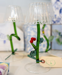 Decorative glass lamp with green stem and red berries on a white surface.