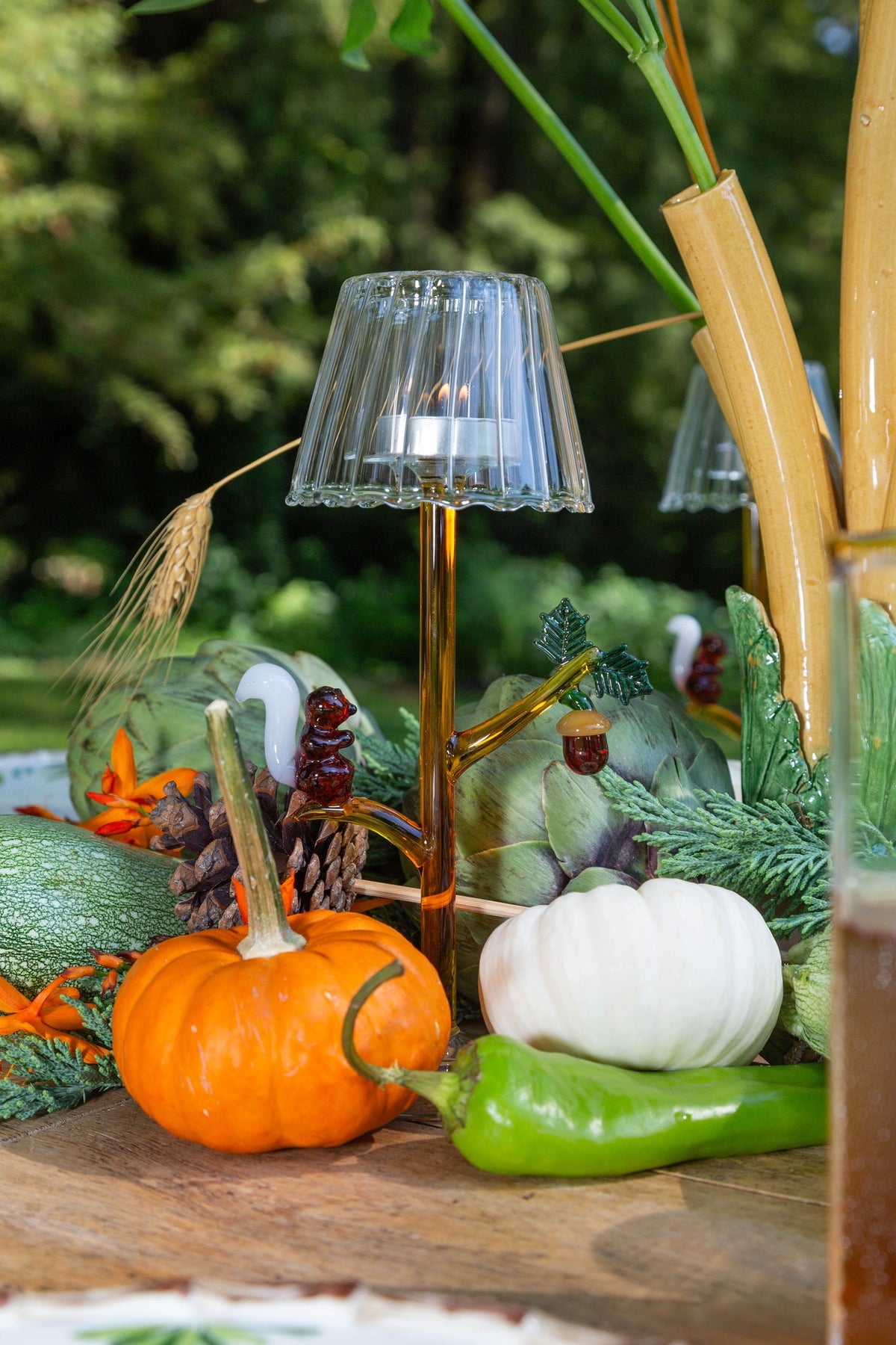 Decorative setup with pumpkins, a small lamp, and greenery on a wooden surface.