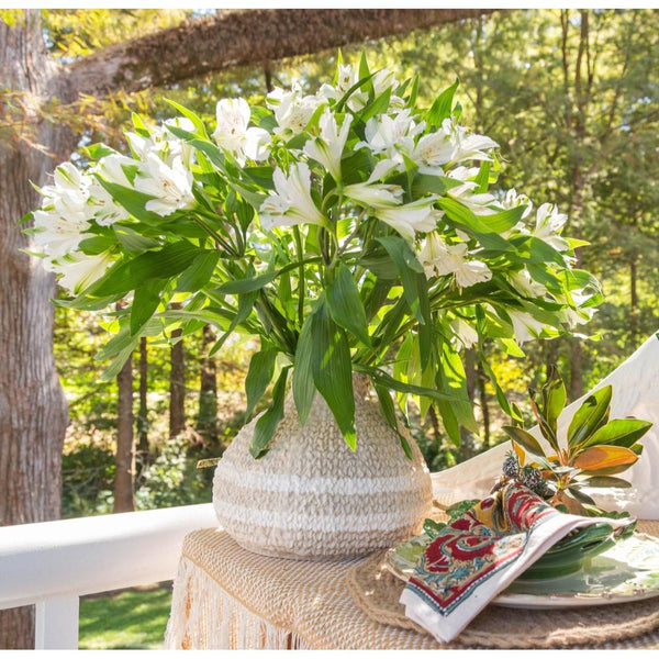 Bouquet of white flowers in a woven vase on a table outdoors with greenery in the background