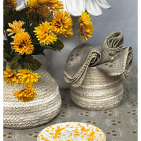 Two woven baskets with a bouquet of yellow flowers and a folded fabric on a patterned surface.