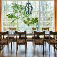 Dining room with large window, Millback Dining Chairs by Woodbridge Furniture, table, greenery vases, black pendant light.