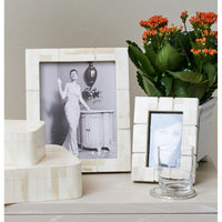 Two Abigails Inlaid Cream + Bone Photo Frames, a glass, and a potted flowering plant on a light table.