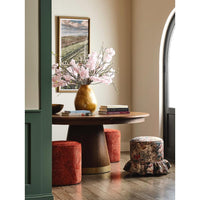 Rawlins Jupe Dining Table by Woodbridge with pink flowers, books, red stools, and a floral ottoman in a cozy room.