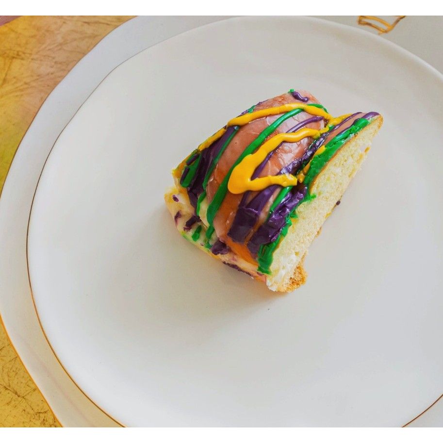 A slice of King Cake sits on an Abigails Gold Rim Crown Dinner Plate (set of 2) with green, yellow, and purple icing.