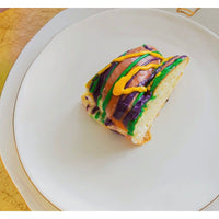 A slice of King Cake sits on an Abigails Gold Rim Crown Dinner Plate (set of 2) with green, yellow, and purple icing.