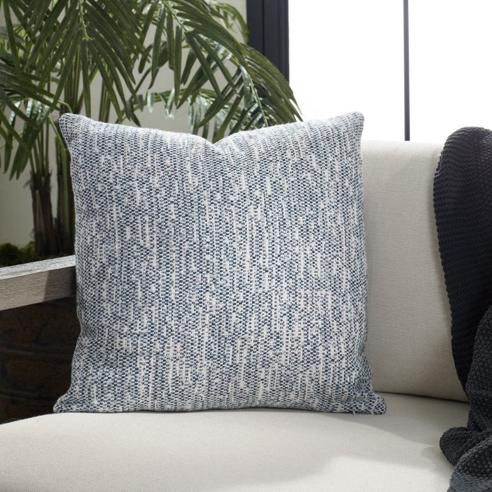 Textured blue pillow on a white couch with a plant in the background