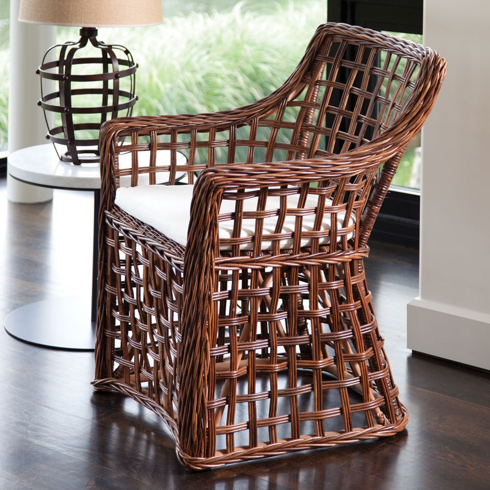 Wicker chair with a white cushion on a wooden floor, with a blurred background of a lamp and window.