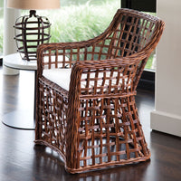 Wicker chair with a white cushion on a wooden floor, with a blurred background of a lamp and window.