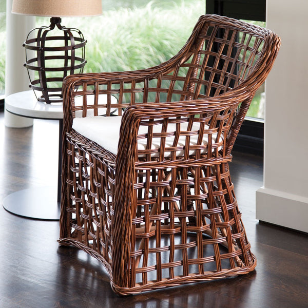 Wicker chair with a white cushion on a wooden floor, with a blurred background of a lamp and window.