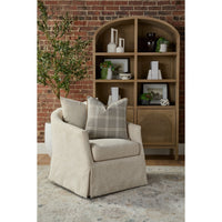 A beige upholstered armchair with two plaid throw pillows, positioned in front of a wooden arched bookcase against a brick wall.