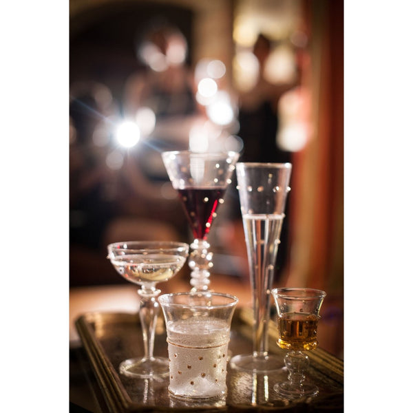 A set of various clear glass champagne glasses decorated with small metallic gold and silver rhinestone accents on a gold tray set against a blurred background