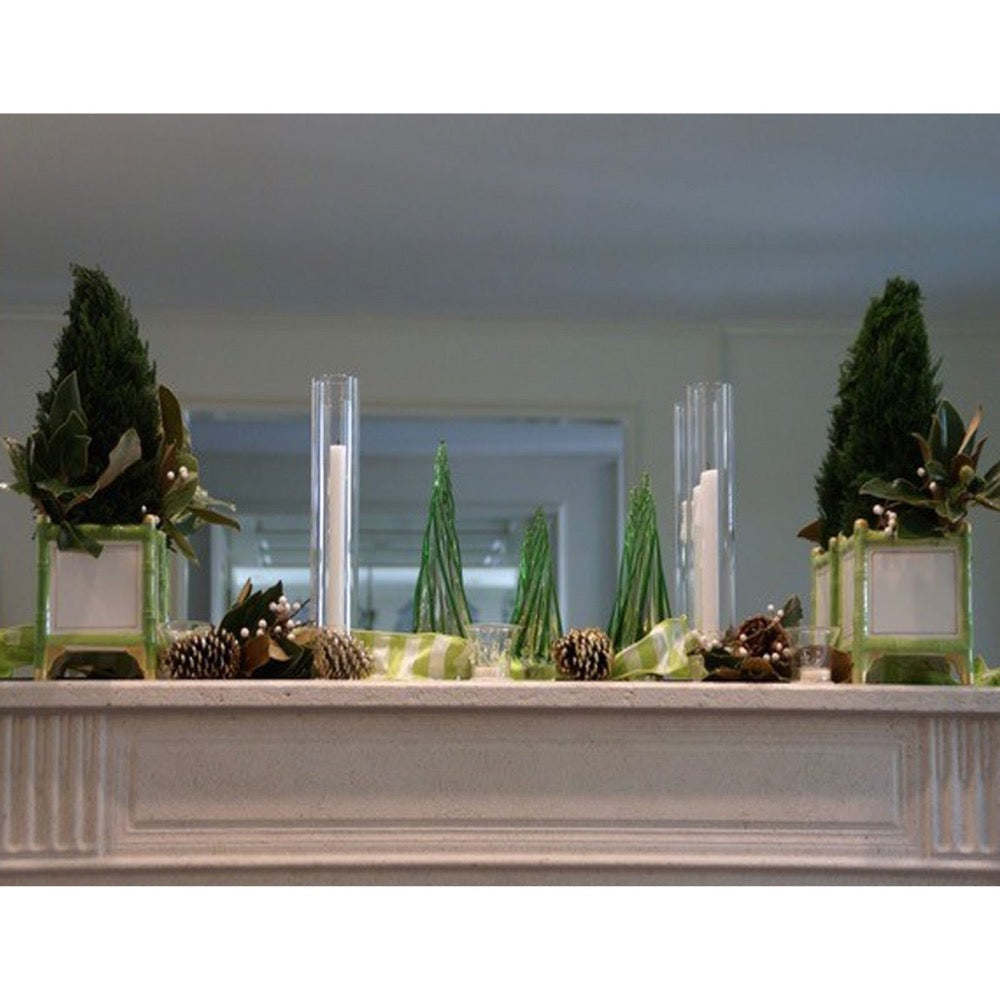 Decorative setup with green trees and candles on a white surface.
