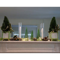 Decorative setup with green trees and candles on a white surface.