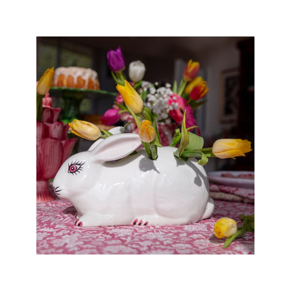White rabbit-shaped vase with flowers on a patterned tablecloth