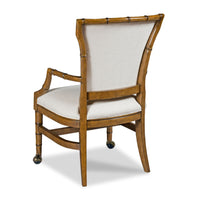 A bamboo-style dining chair with a warm brown wood frame, upholstered in light beige fabric on the seat and backrest, and small dark metal caster wheels at the base, shown on a white background.