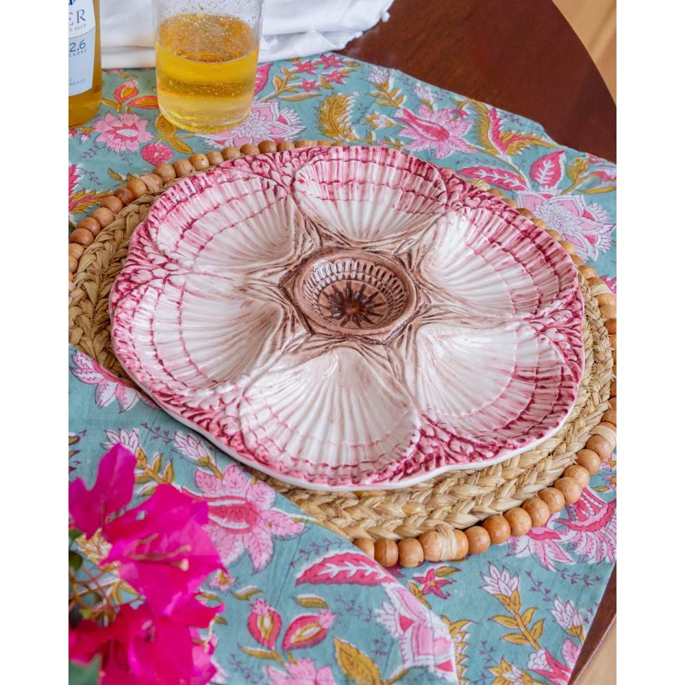 A ceramic five-piece serving platter with a pink and white floral shell design, displayed on a woven placemat over a turquoise floral tablecloth.