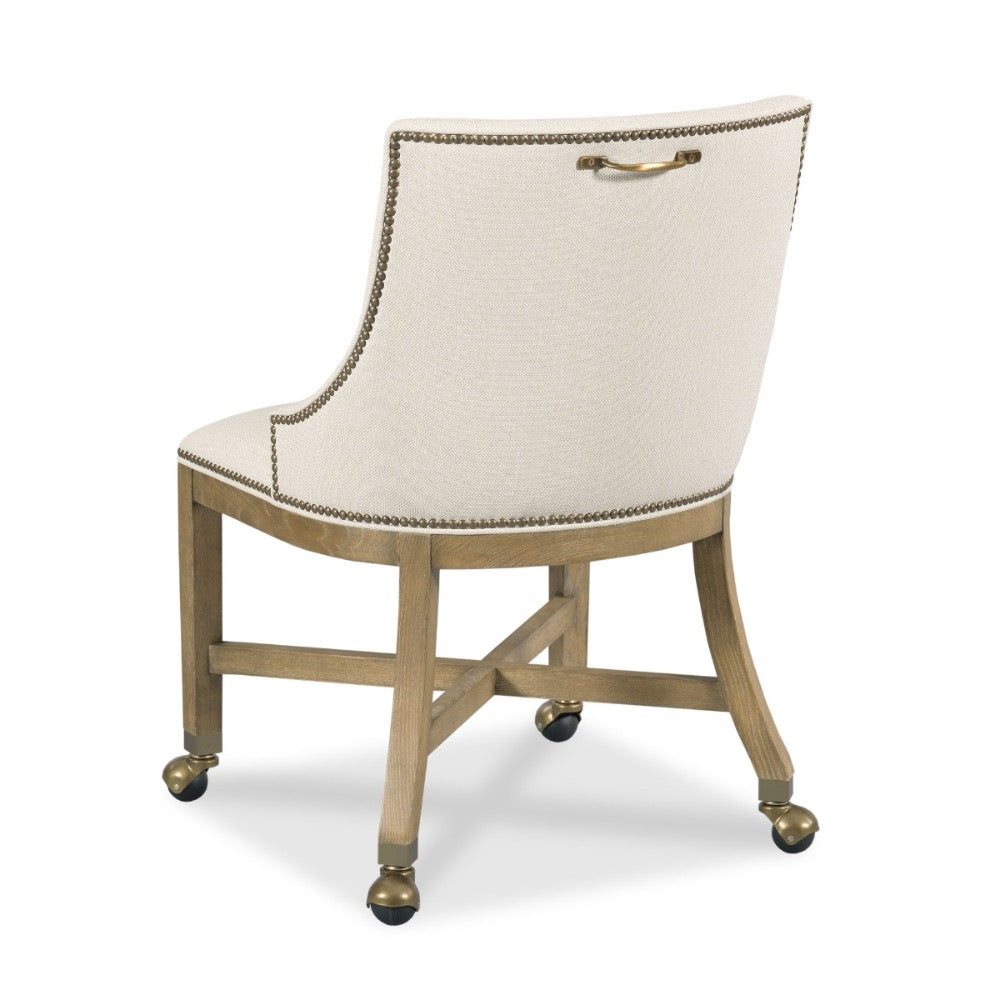 An upholstered accent chair with a cream textured fabric seat and backrest, gold nailhead trim, and a curved light wood frame with brass hardware and casters.