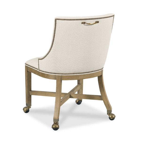 An upholstered accent chair with a cream textured fabric seat and backrest, gold nailhead trim, and a curved light wood frame with brass hardware and casters.