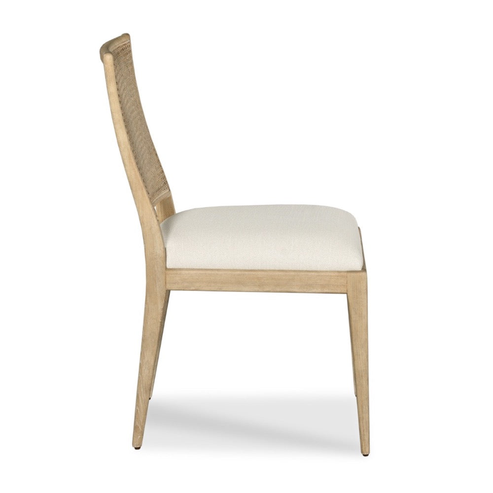 A single dining chair shown from the side against a plain white background. The chair has a light natural wood frame and legs, a woven cane backrest, and a light beige upholstered seat cushion.