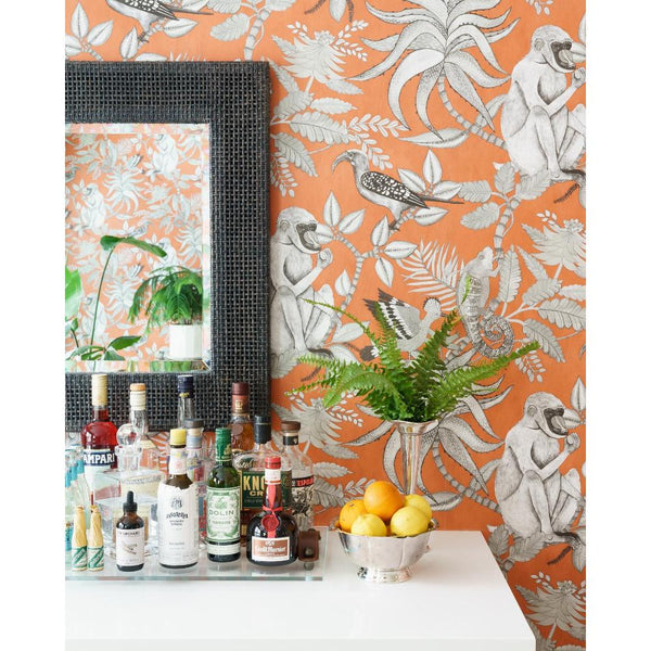 A bar cart sits by orange monkey wallpaper and a Made Goods Isla Smoked Peeled Rattan Mirror.